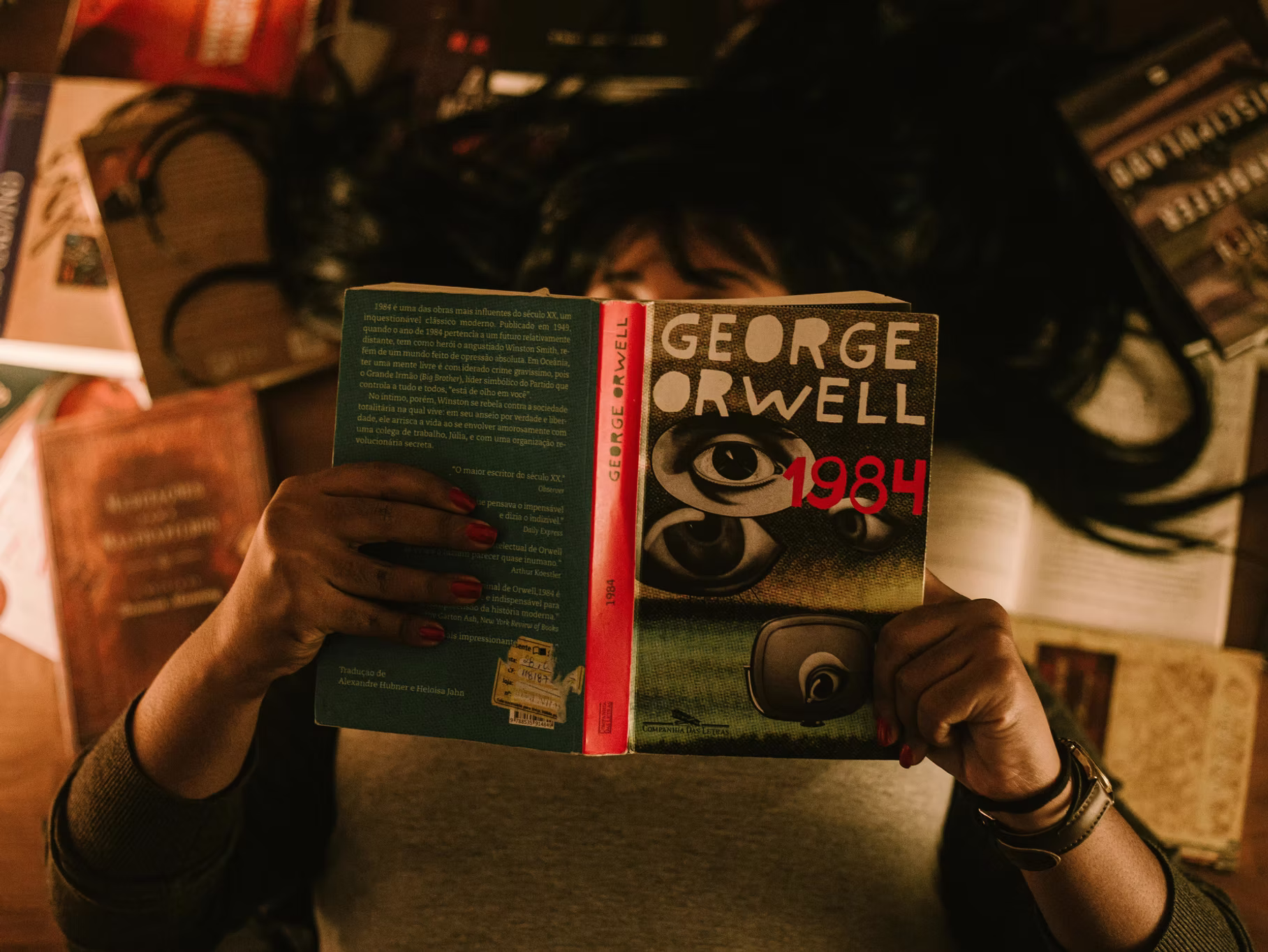Person reading George Orwell's "1984" surrounded by various books, illustrating a deep engagement with literature and themes of surveillance and society.