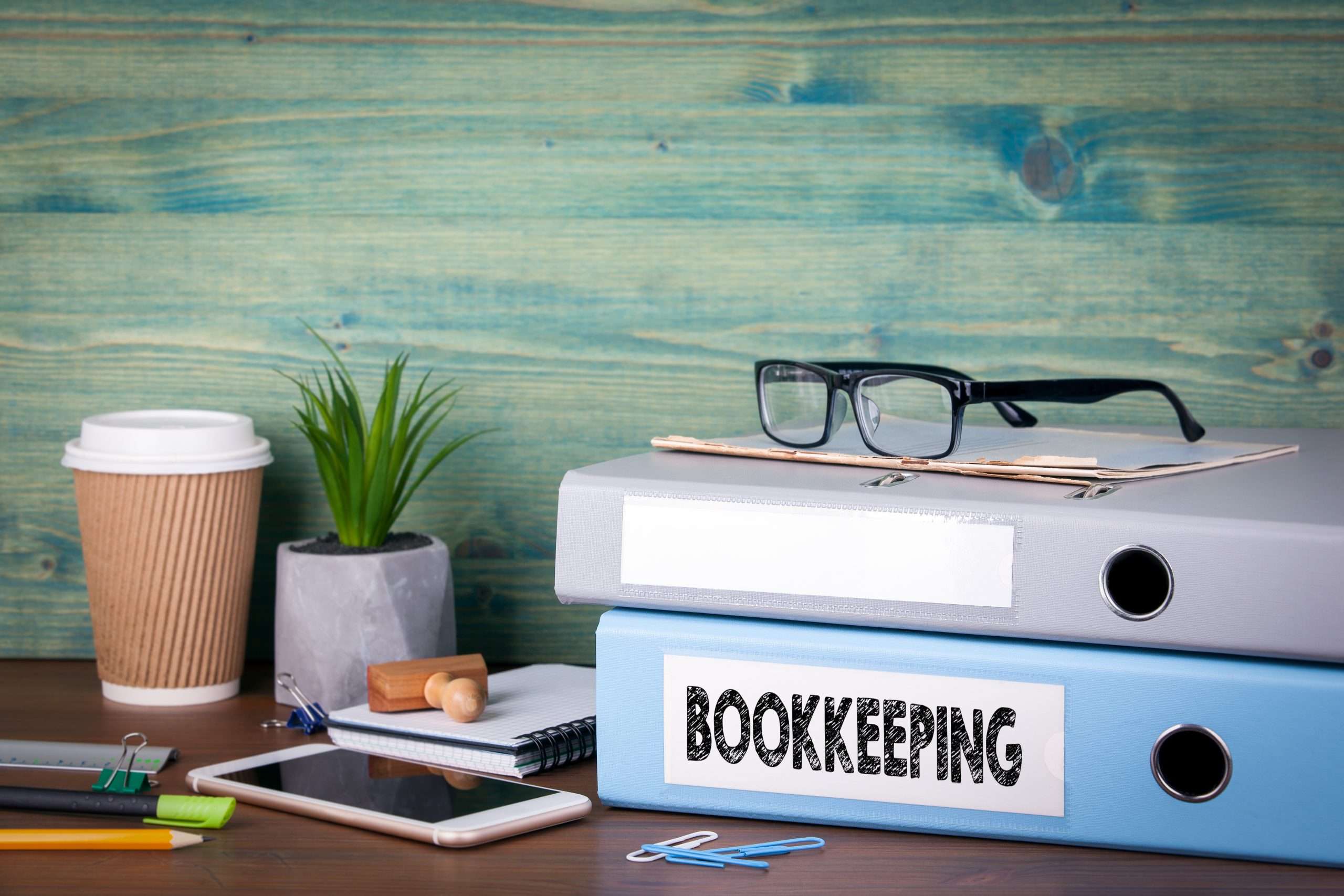 Bookkeeping binders, glasses, and stationery on a wooden desk, emphasizing organized financial recordkeeping for business management.