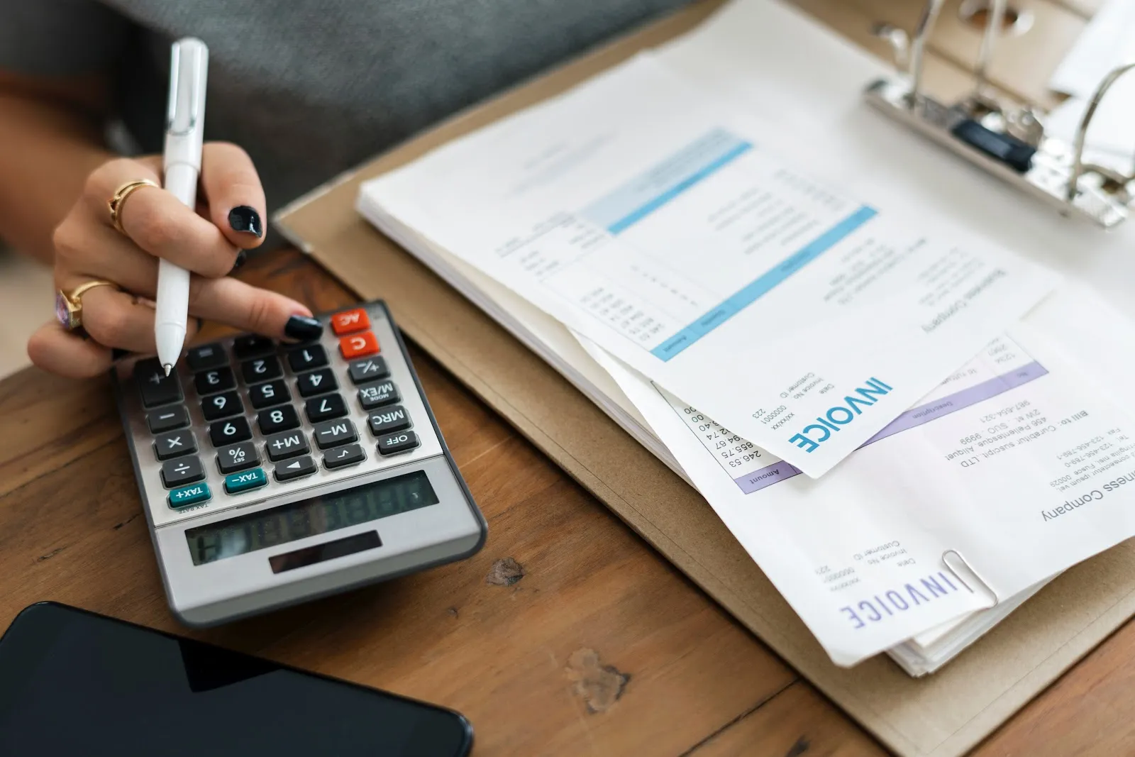 Person using a calculator while reviewing invoices, symbolizing bookkeeping services for small to mid-sized businesses.