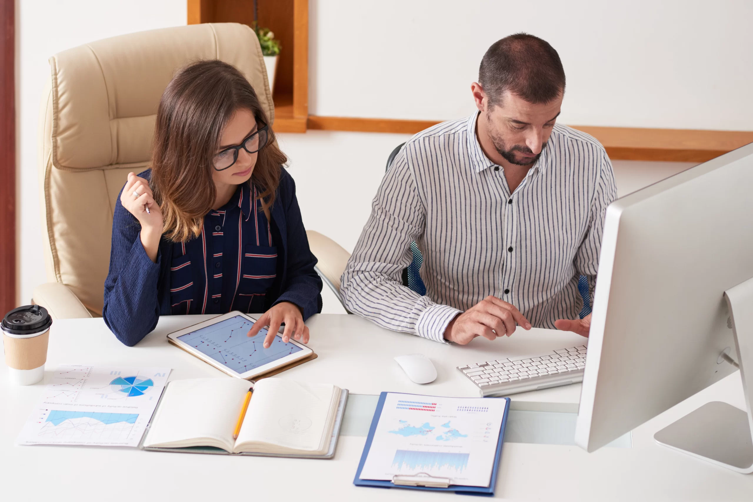 Professional team analyzing financial data on tablet and computer in an office setting, surrounded by financial reports and documents, reflecting bookkeeping and reporting services.